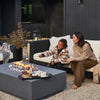 Concrete fire pit table with flames rising between ceramic spheres, set on a patio beside outdoor seating
