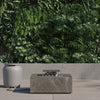 Square OuterStone fire pit table on a patio beside its stone-topped propane tank cover